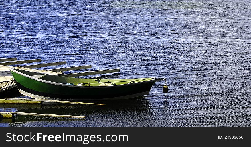 An isolated rowboat tied to a dock floating in blue waters of a lake. An isolated rowboat tied to a dock floating in blue waters of a lake