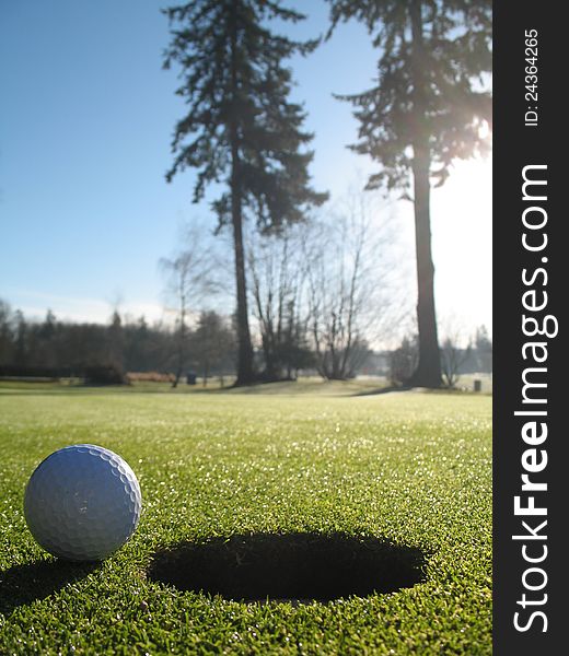 Photo of golf ball on the green beside the hole.