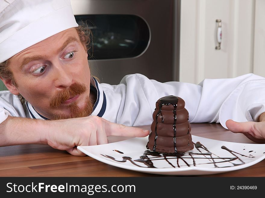 Funny young chef strange looking at piece of cake with chocolate sauce