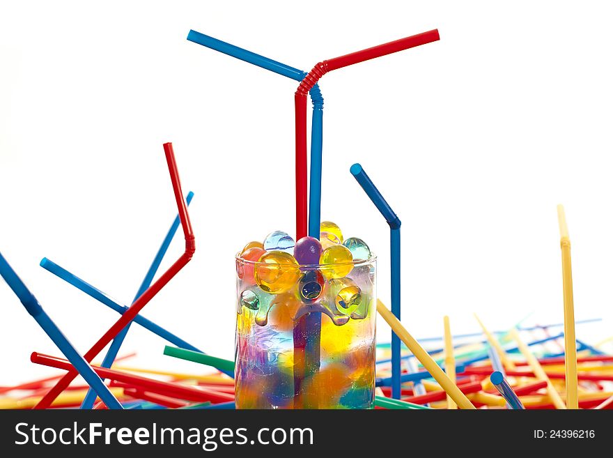 Multicolored straws and a  glass with silicone balls on white ground. Multicolored straws and a  glass with silicone balls on white ground