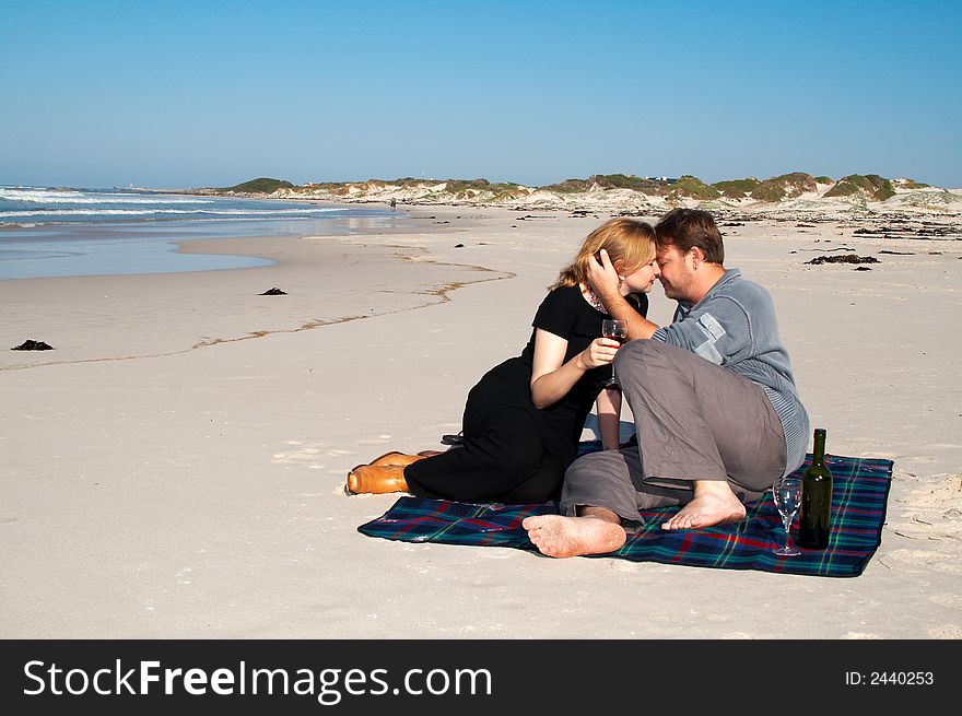 Young married couple moving closer to each other for a kiss. They are enjoying their winter vacation on the beach in South Africa. Shot on a sunny day with blue skies and ocean full of waves in the background. Young married couple moving closer to each other for a kiss. They are enjoying their winter vacation on the beach in South Africa. Shot on a sunny day with blue skies and ocean full of waves in the background.