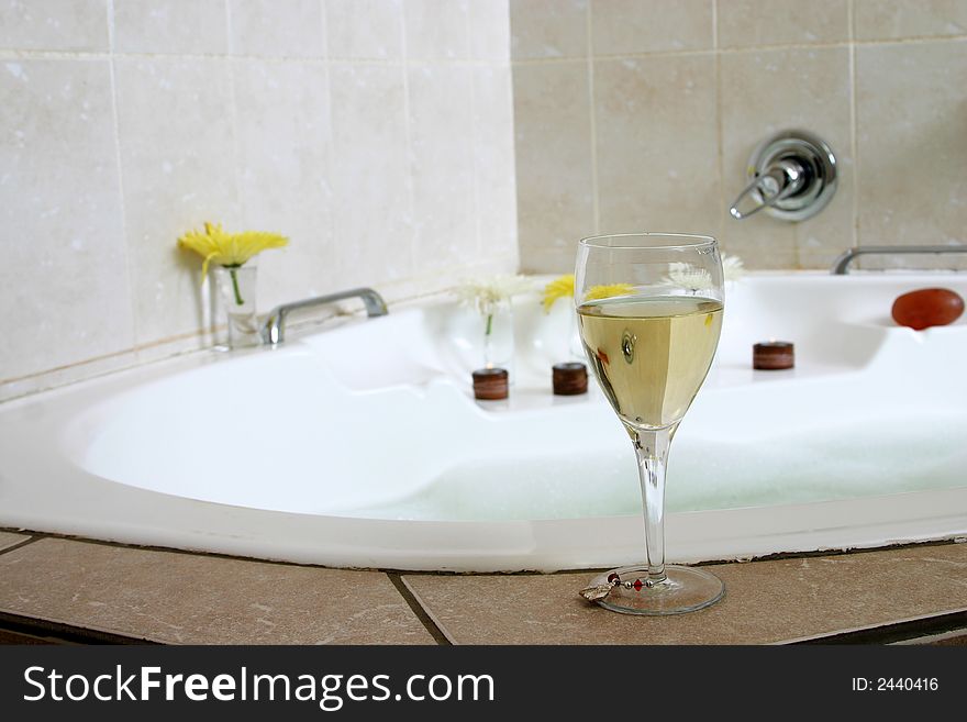Glass of champagne standing on white bath-tub, decorated with flowers and candles. Glass of champagne standing on white bath-tub, decorated with flowers and candles.