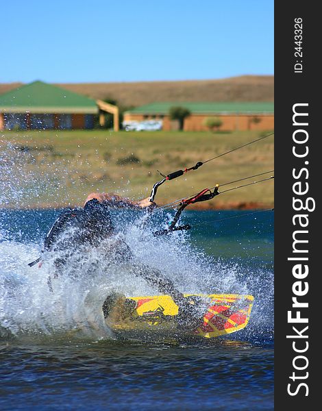A kitesurfer on inlnad dam with building behind, with his hand in the water causing a large spray. A kitesurfer on inlnad dam with building behind, with his hand in the water causing a large spray
