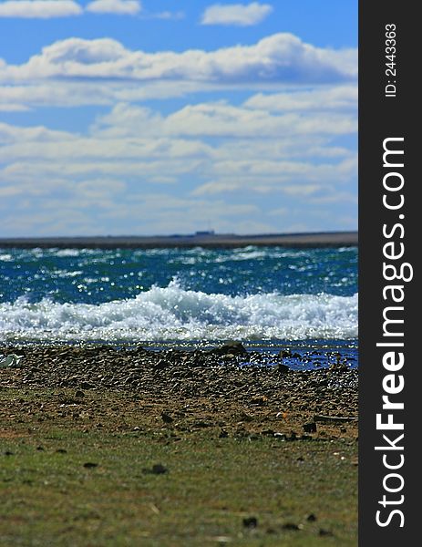 A dam, grass, rocks and stones; water; waves; swells; wall and sky on a windy day. A dam, grass, rocks and stones; water; waves; swells; wall and sky on a windy day