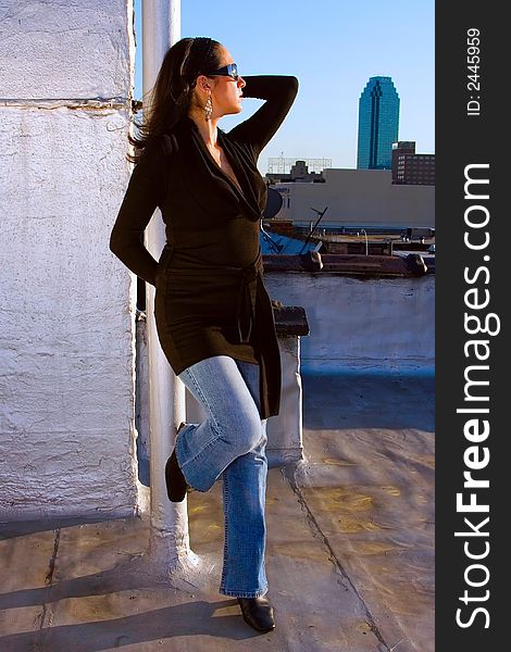 A woman posing as a fashion model in a black long shirt and jeans. She's wearing sunglasses and is holding up one arm. There's a skyscraper in the background.