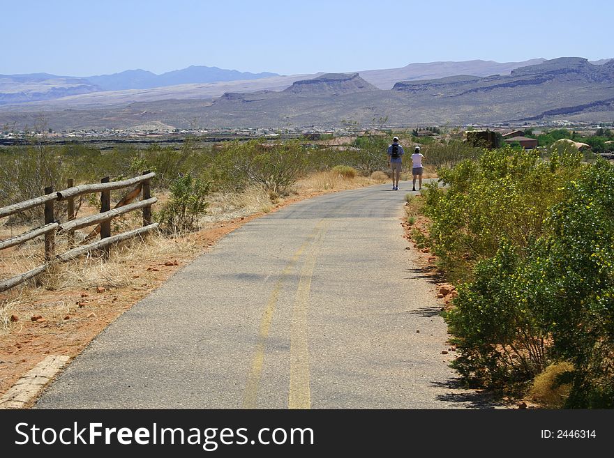 Couple walking down a hiking trail toward town.
Mountains on the horizon. Clear blue sky. Couple walking down a hiking trail toward town.
Mountains on the horizon. Clear blue sky.