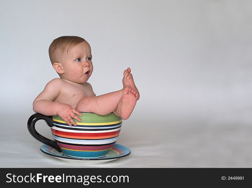 Image of an adorable baby sitting in a colorful, over-sized teacup. Image of an adorable baby sitting in a colorful, over-sized teacup