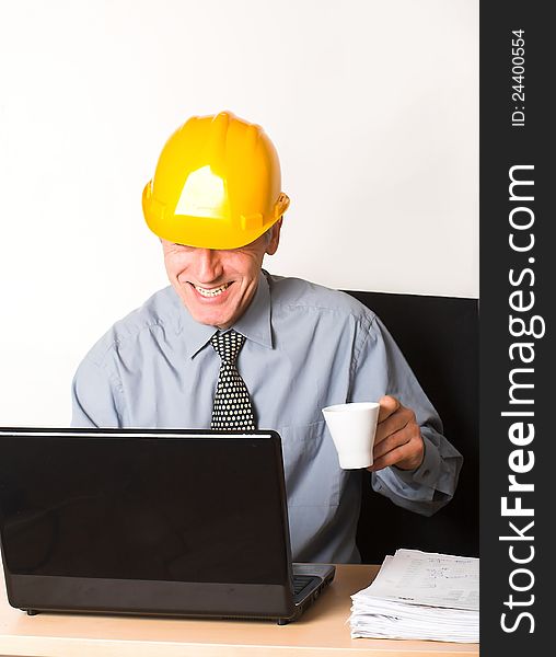 White employee, wearing yellow helmet, blue shirt and tie, plays games on his laptop. White employee, wearing yellow helmet, blue shirt and tie, plays games on his laptop.