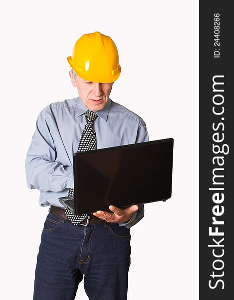 Matured, white employee, wearing yellow helmet, blue shirt and tie, stands and works on his laptop. Matured, white employee, wearing yellow helmet, blue shirt and tie, stands and works on his laptop.