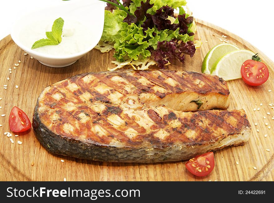 Salmon steak cooking on the grill with fresh herbs and sauce