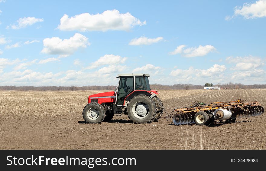 Red farm tractor with a plow in a farm field. Red farm tractor with a plow in a farm field