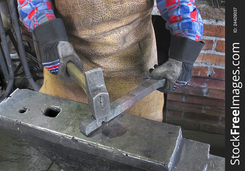 Hands and arms of a blacksmith working with tools, wearing heavy gloves and a leather apron.