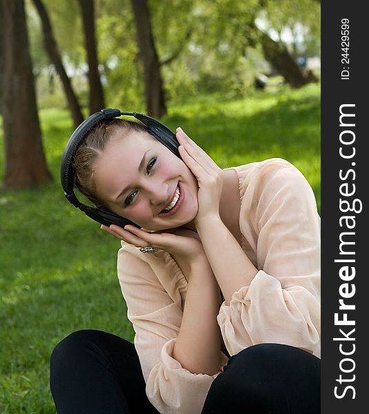 Happy Woman Sitting On Grass Listening To Music