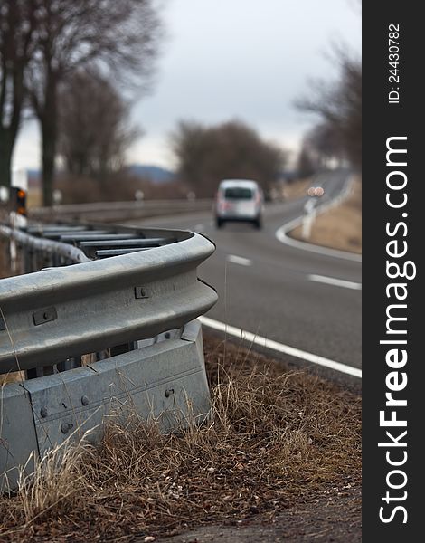 View of a crash barrier with the traffic on a country road blurred in the background. View of a crash barrier with the traffic on a country road blurred in the background