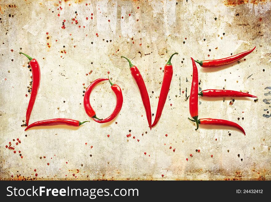 Red hot chili peppers arranged to the word LOVE on an attractive grunge background with peppercorns. Red hot chili peppers arranged to the word LOVE on an attractive grunge background with peppercorns