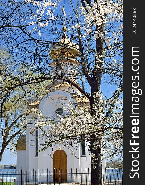 A chapel at a riverbank under april blue sky and with f blooming tree
