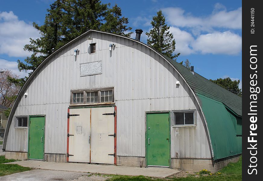 Front of an old Quonset hut building with a white front, green doors and roof.