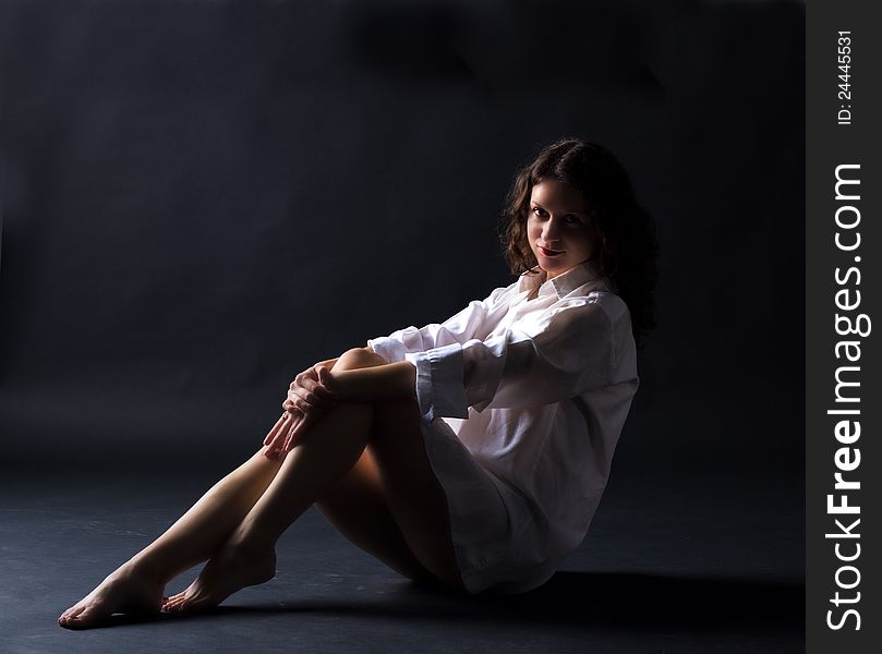 Young girl in white shirt posing sitting in studio on dark background