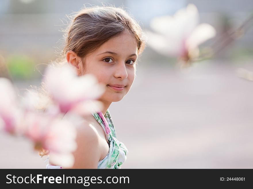 Beautiful young girl looks between blurred magnolia blossoms. Beautiful young girl looks between blurred magnolia blossoms