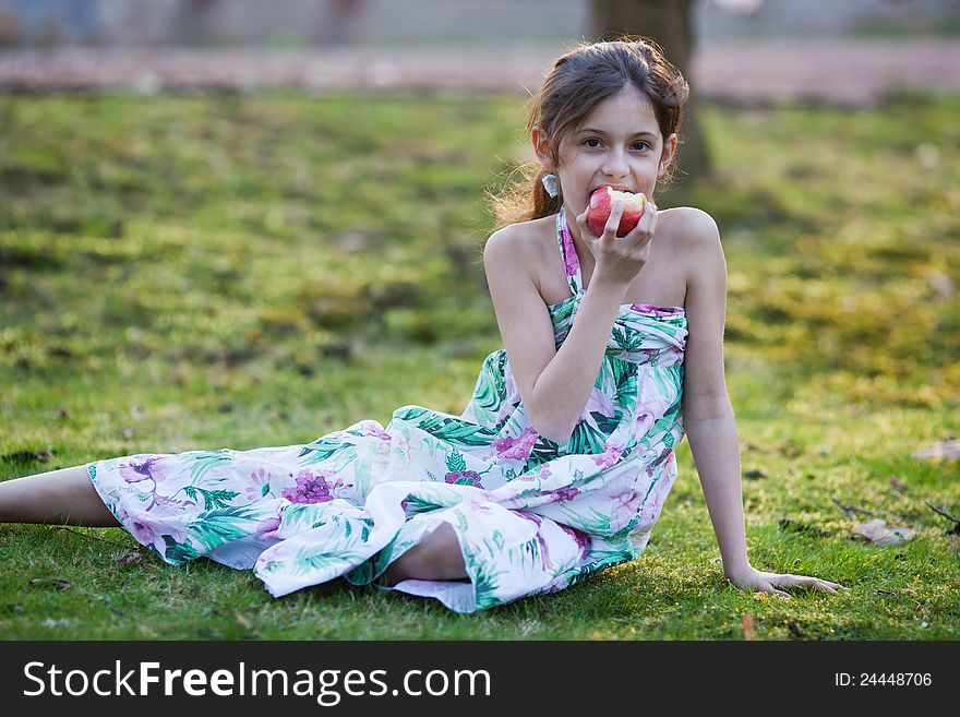 Beautiful young girl sits on a meadow and eats a red apple. Beautiful young girl sits on a meadow and eats a red apple