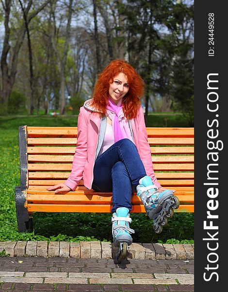 Young ginger girl on roller stakes sitting on the bench in the park in sunny day. Young ginger girl on roller stakes sitting on the bench in the park in sunny day