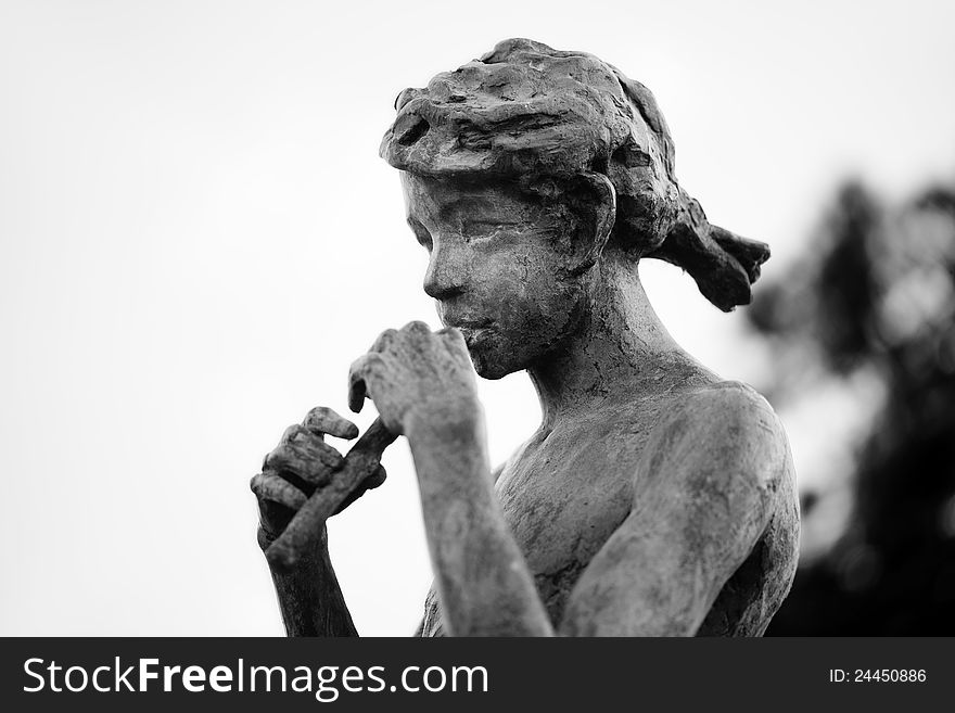 Old bronze statue of girl playing a flute. Black and white photo with shallow depth of field.