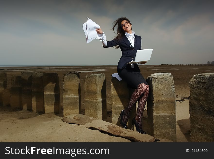 Business lady sitting on the beach, on a background cloudy sky. She sits on the pile, the wind fluttering her hair. In the hands of her laptop.