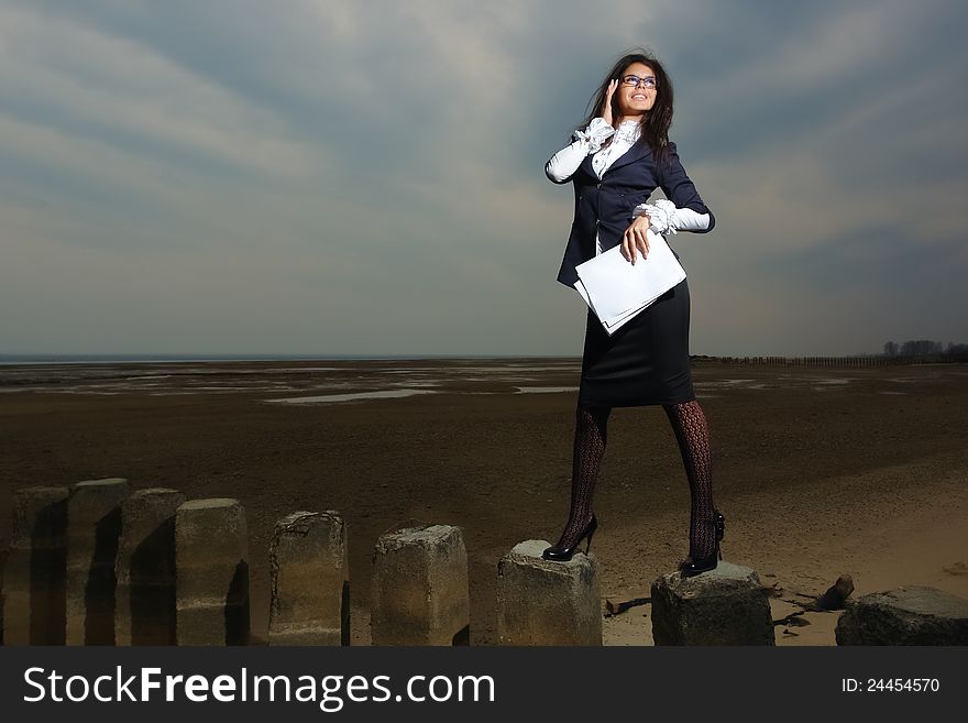 Business lady standing on the beach, on a background cloudy sky. It stands on stilts, the wind fluttering her hair. In the hands of her paper.