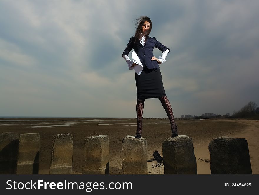 Business lady standing on the beach, on a background cloudy sky. It stands on stilts, the wind fluttering her hair. In the hands of her paper.