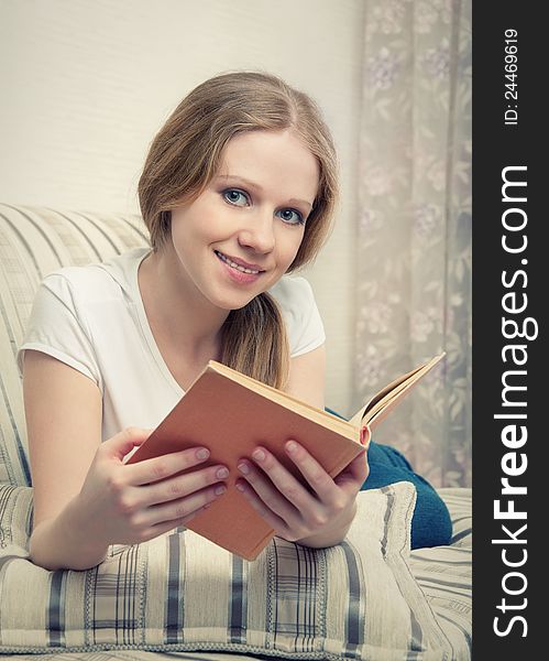 Pretty girl reading a book lying on the sofa