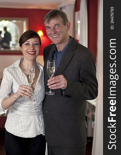 Happy smiling romantic couple standing side by side with champagne glasses in their hands in romantic red interior.