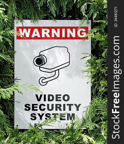 Video security system warning signboard on a fence hedge. Video security system warning signboard on a fence hedge
