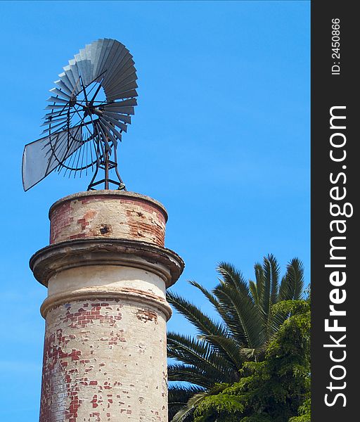 Windmill water pump on top of a brick built tower with vegetation and a blue sky. Windmill water pump on top of a brick built tower with vegetation and a blue sky