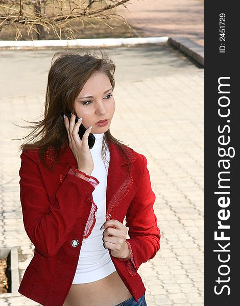 The young woman in a red jacket speaks by phone. The young woman in a red jacket speaks by phone.