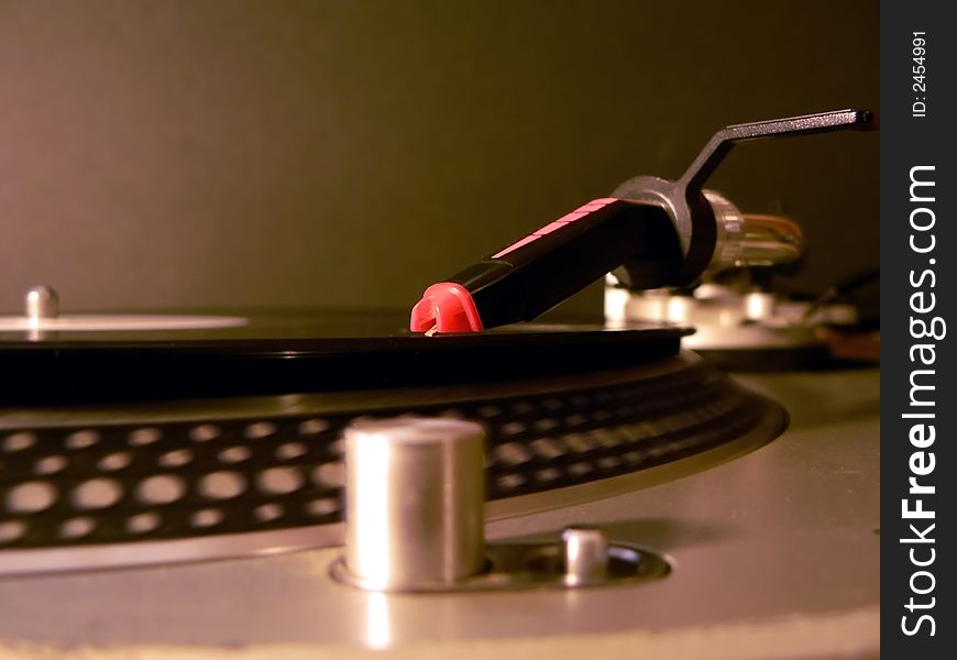 Photo of dj turntable needle on record with the focus on the needle illuminated under party lights.