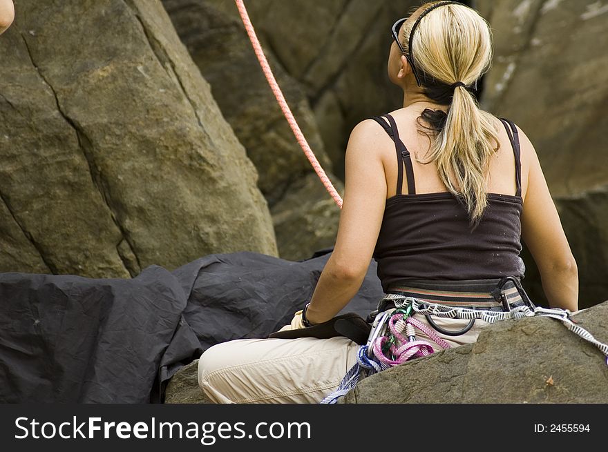 A rock climber woman seating and looking up at a cliff