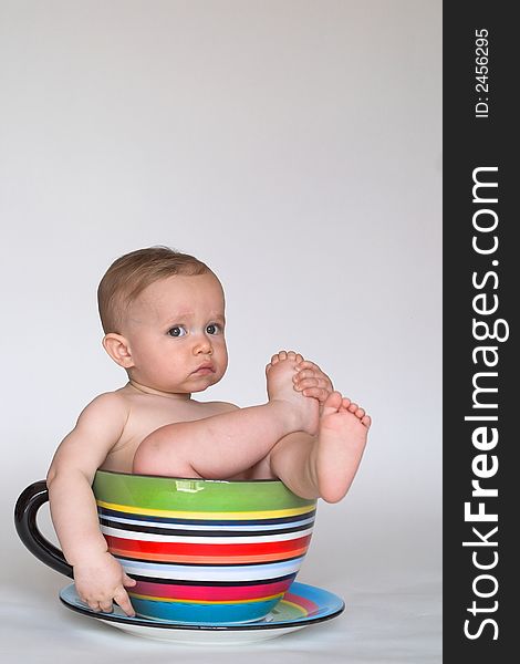 Image of an adorable baby sitting in a colorful, over-sized teacup. Image of an adorable baby sitting in a colorful, over-sized teacup