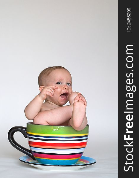 Image of an adorable baby sitting in a colorful, over-sized teacup. Image of an adorable baby sitting in a colorful, over-sized teacup
