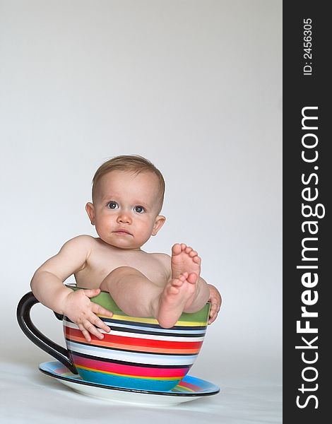 Image of an adorable baby sitting in a colorful, over-sized teacup. Image of an adorable baby sitting in a colorful, over-sized teacup