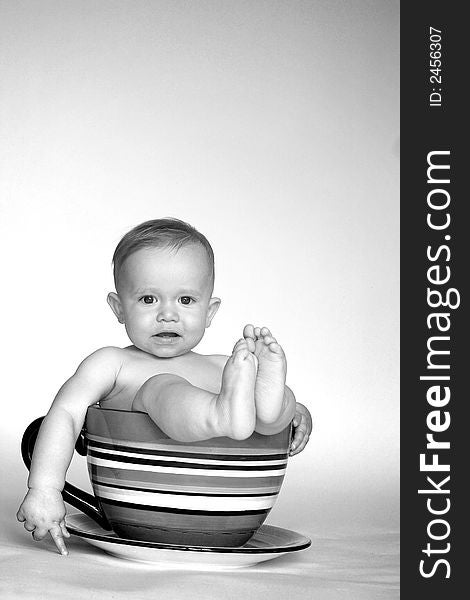 Black and white image of cute baby sitting in an over-sized teacup. Black and white image of cute baby sitting in an over-sized teacup