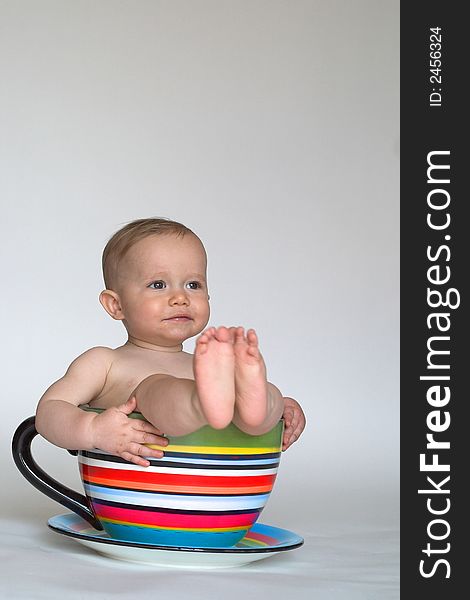 Image of an adorable baby sitting in a colorful, over-sized teacup. Image of an adorable baby sitting in a colorful, over-sized teacup