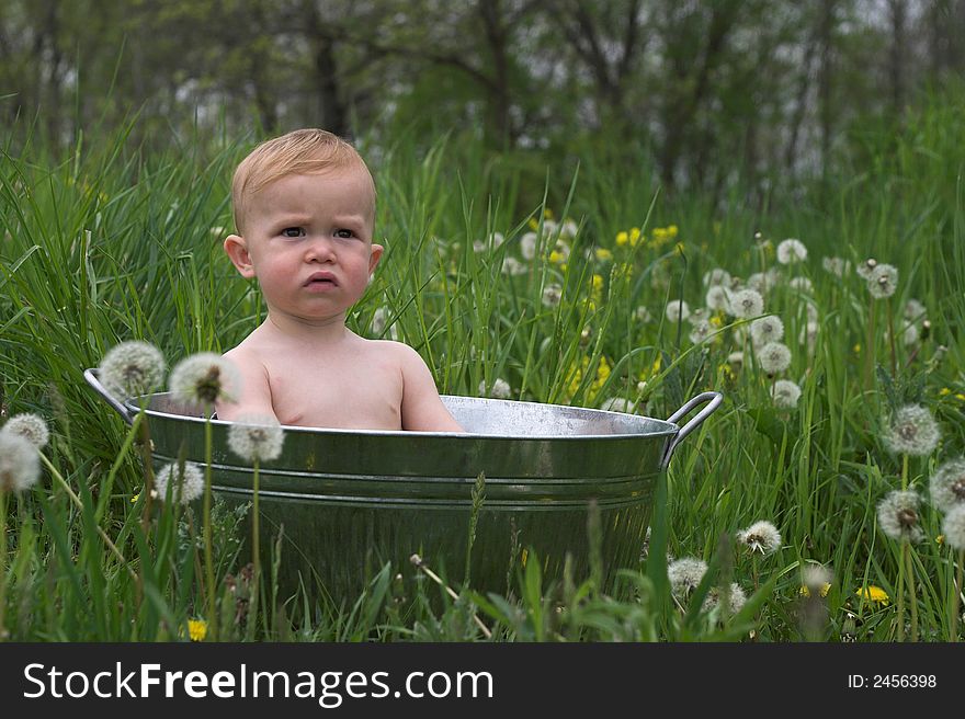 Image of a cute baby sitting in a galvanized tub in a meadow. Image of a cute baby sitting in a galvanized tub in a meadow