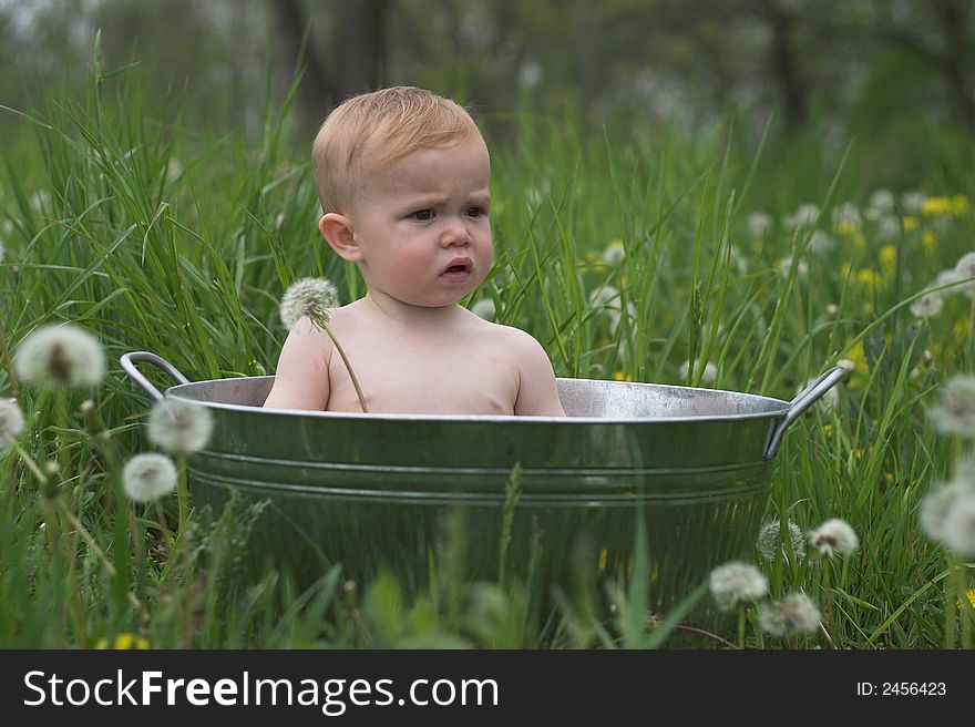 Image of a cute baby sitting in a galvanized tub in a meadow. Image of a cute baby sitting in a galvanized tub in a meadow