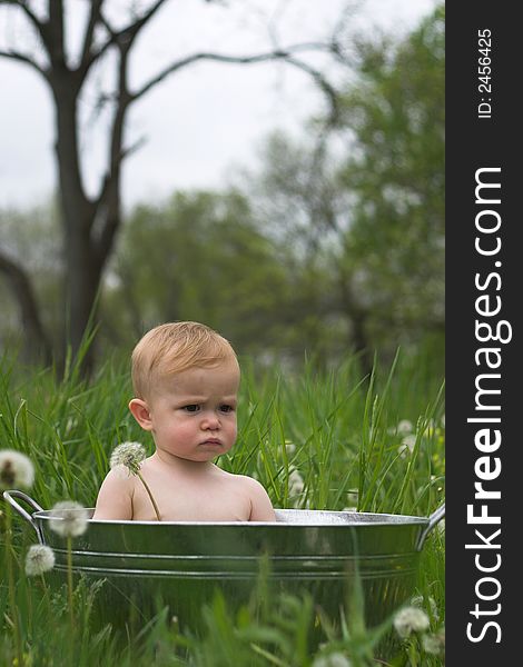 Image of a cute baby sitting in a galvanized tub in a meadow. Image of a cute baby sitting in a galvanized tub in a meadow