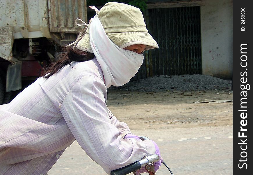 Lady riding bike, covered up from sun and pollution in Vietnam