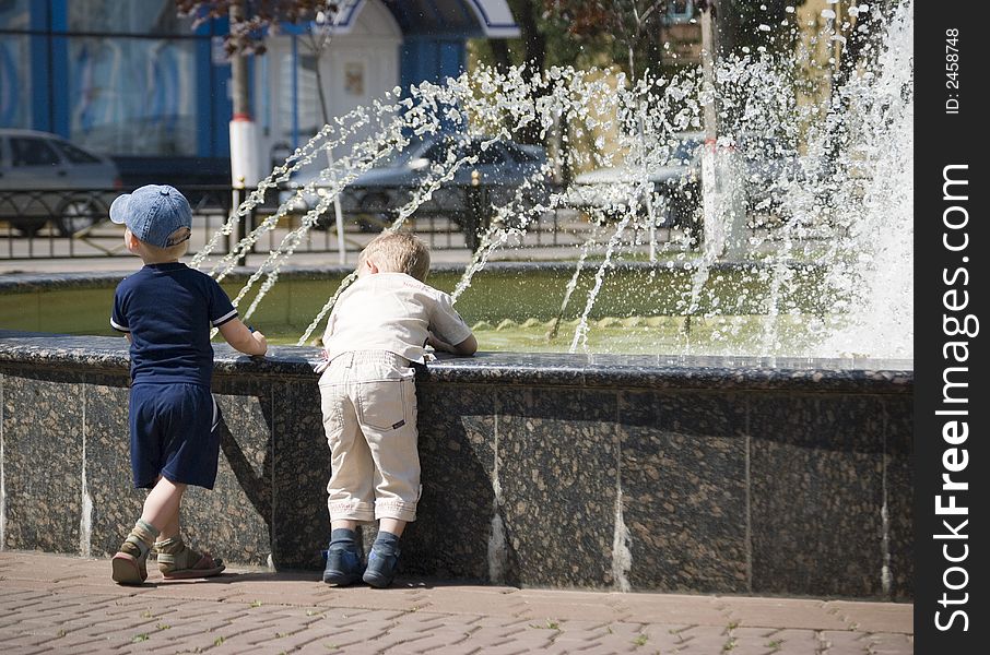 Two boys are watching water sprays at a fountain. Two boys are watching water sprays at a fountain