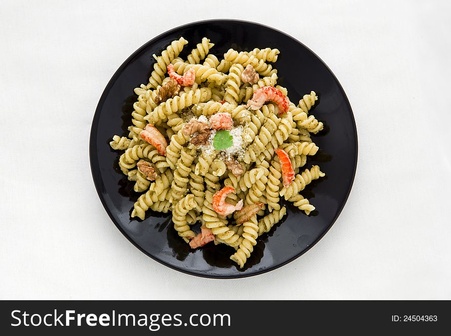 A black dish with pasta with pesto on white table. A black dish with pasta with pesto on white table