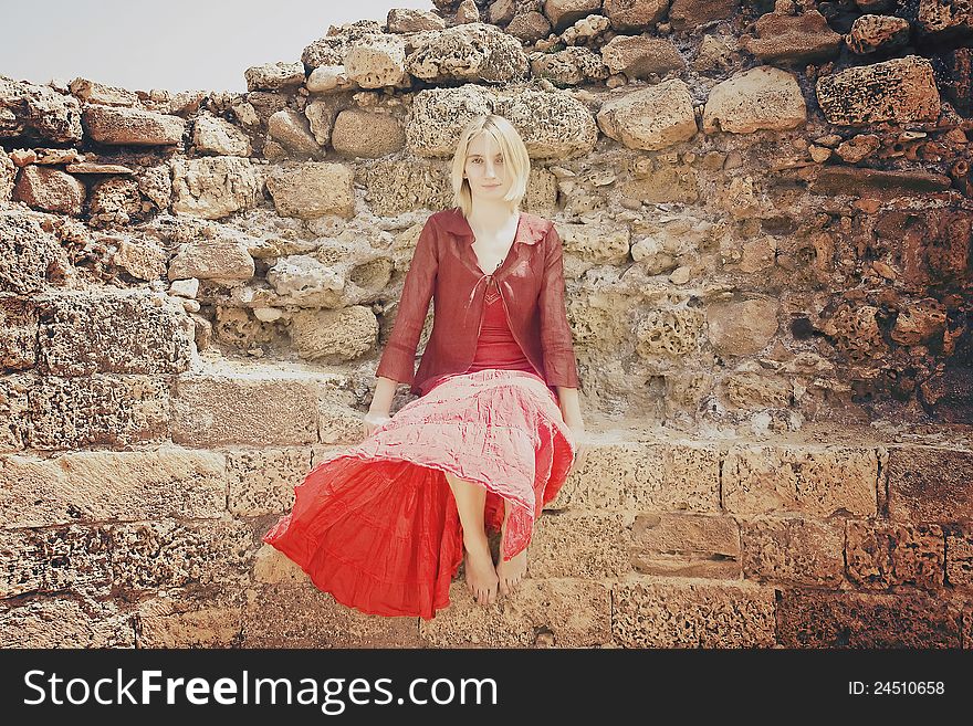 Beautiful young girl in red clothes sitting on the old stone wall. Beautiful young girl in red clothes sitting on the old stone wall.