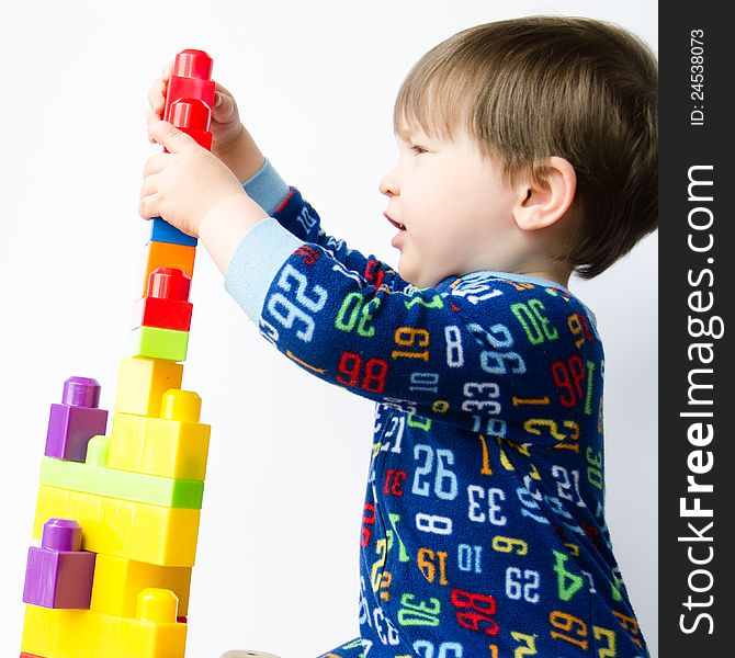 A two-year-old caucasian boy has fun while building a large tower with colorful plastic blocks on a white background. A two-year-old caucasian boy has fun while building a large tower with colorful plastic blocks on a white background.