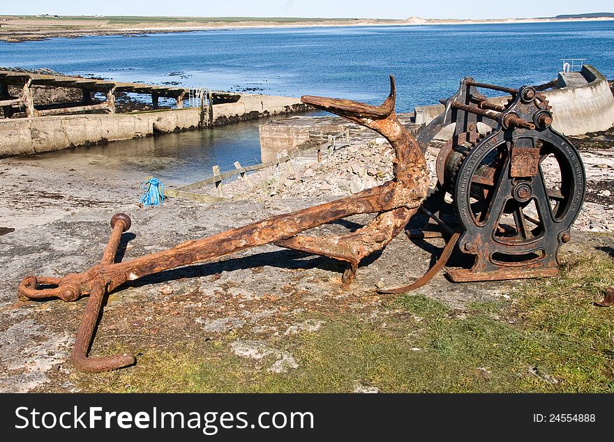 Anchor and a winch,Sinclair Bay, Auckergill, Caithness, Scotland,UK. An anchor windlass is a machine that restrains and manipulates the anchor chain on a boat, allowing the anchor to be raised and lowered by means of chain cable. A notched wheel engages the links of the chain or the rope. Crown-The pointed end of the anchor which attaches the shank to the arms. Eye-Hole at the end of the shank through which the ring is attached. Fluke-The spade-shaped appendage of the arm used for digging into the sea bed to secure the vessel. The palm-Flat uppermost portion of the fluke. A deadman anchor is a buried object like a log, rock, or pack. The strength of the deadman anchor depends on The perpendicular cross-sectional area of the object that is buried. Anchor and a winch,Sinclair Bay, Auckergill, Caithness, Scotland,UK. An anchor windlass is a machine that restrains and manipulates the anchor chain on a boat, allowing the anchor to be raised and lowered by means of chain cable. A notched wheel engages the links of the chain or the rope. Crown-The pointed end of the anchor which attaches the shank to the arms. Eye-Hole at the end of the shank through which the ring is attached. Fluke-The spade-shaped appendage of the arm used for digging into the sea bed to secure the vessel. The palm-Flat uppermost portion of the fluke. A deadman anchor is a buried object like a log, rock, or pack. The strength of the deadman anchor depends on The perpendicular cross-sectional area of the object that is buried.
